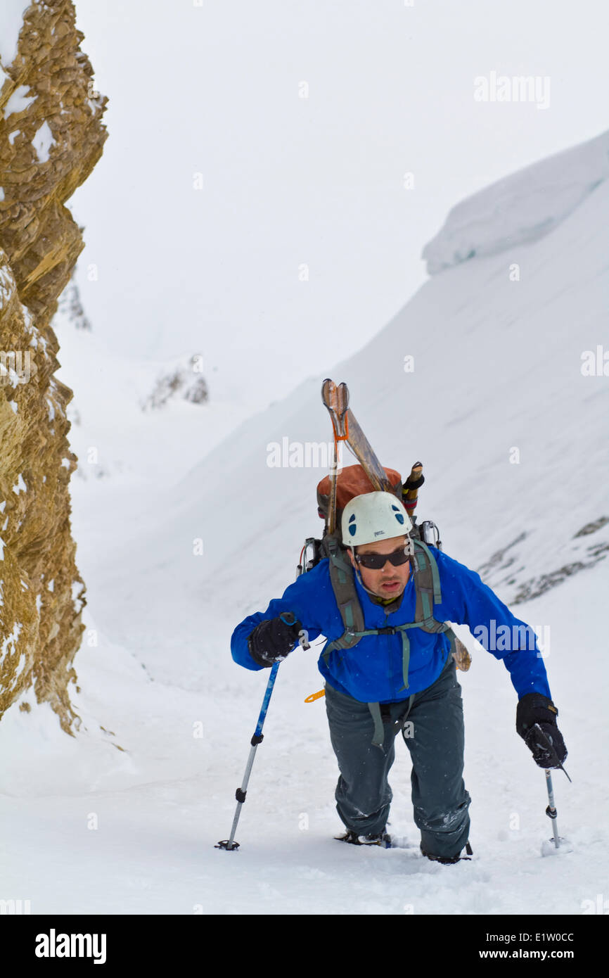 A male backcountry skier bootpacks up a steep couloir on Mt. Chester, Kananaskis, AB Stock Photo