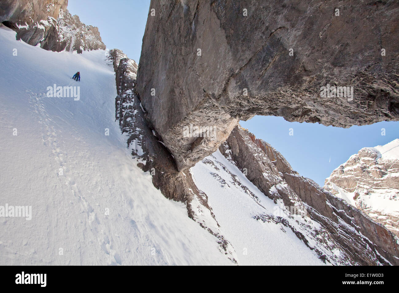 A male backcountry skier bootpacks up a steep couloir with a unique limestone arch in it. Mt. French Peter Lougheed Provincial Stock Photo