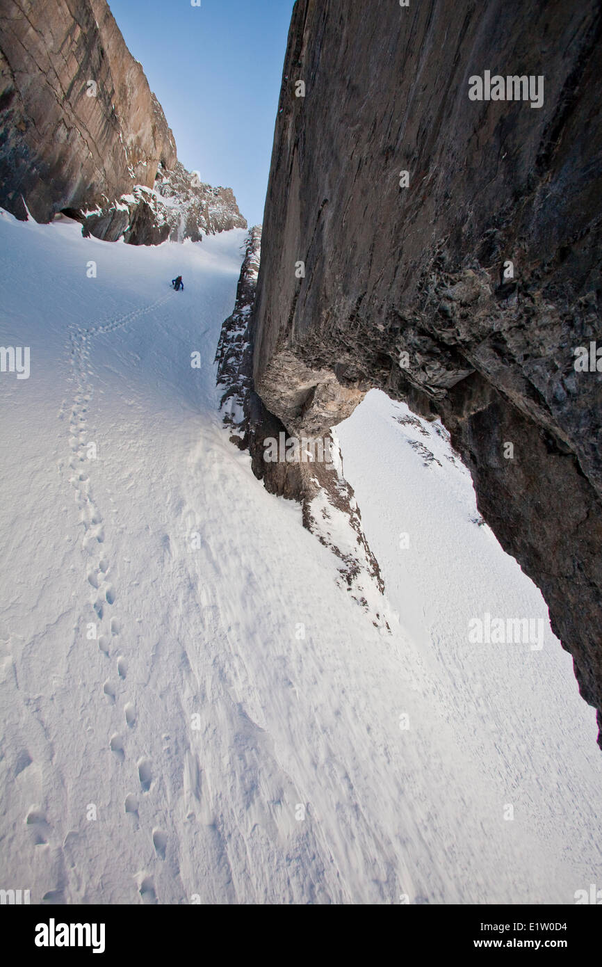 A male backcountry skier bootpacks up a steep couloir with a unique limestone arch in it. Mt. French Peter Lougheed Provincial Stock Photo