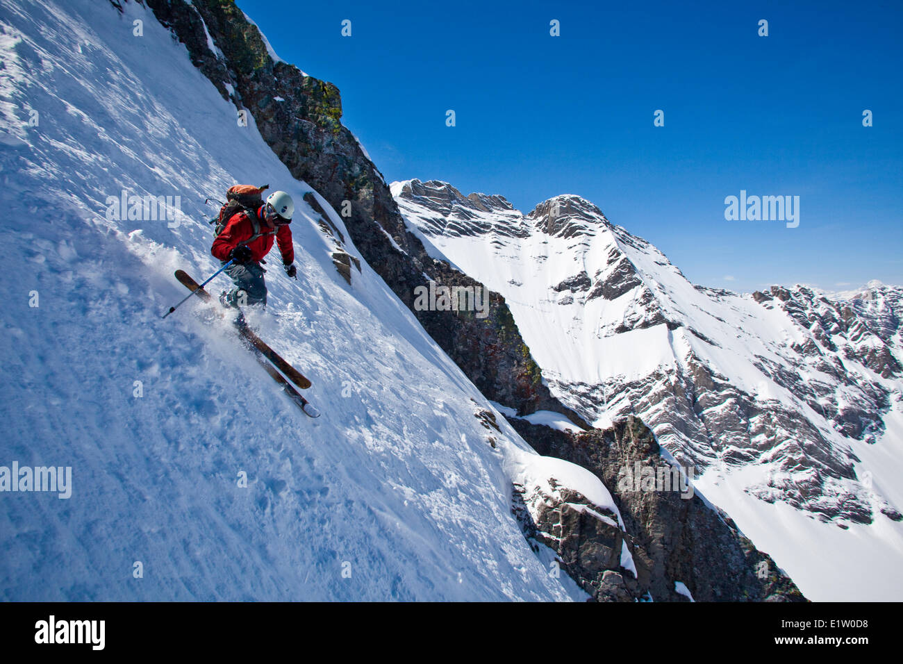 A male backcountry skier on tele skis descends a steep couloir with a