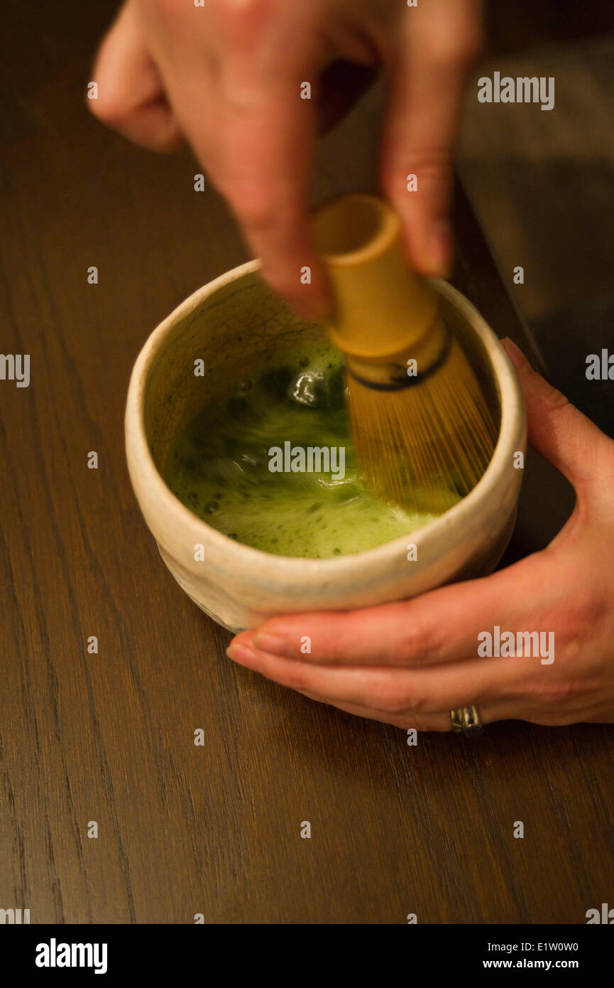 Woman preparating Japanese matcha tea in a cup with a whisk Stock Photo