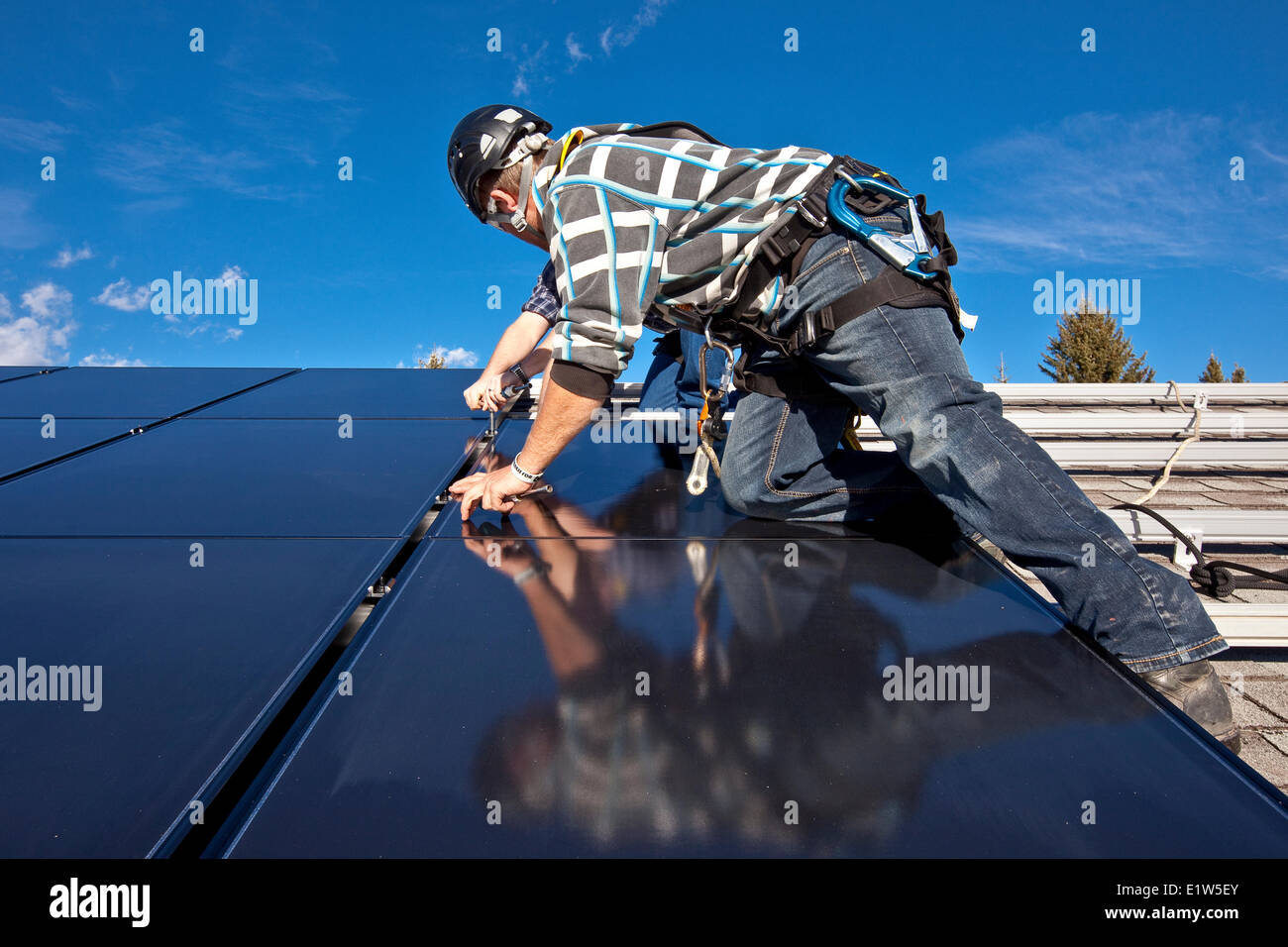 Two solar panel installers install solar panels on roof, Alberta foothills near Black Diamond, Alberta, Canada. Stock Photo