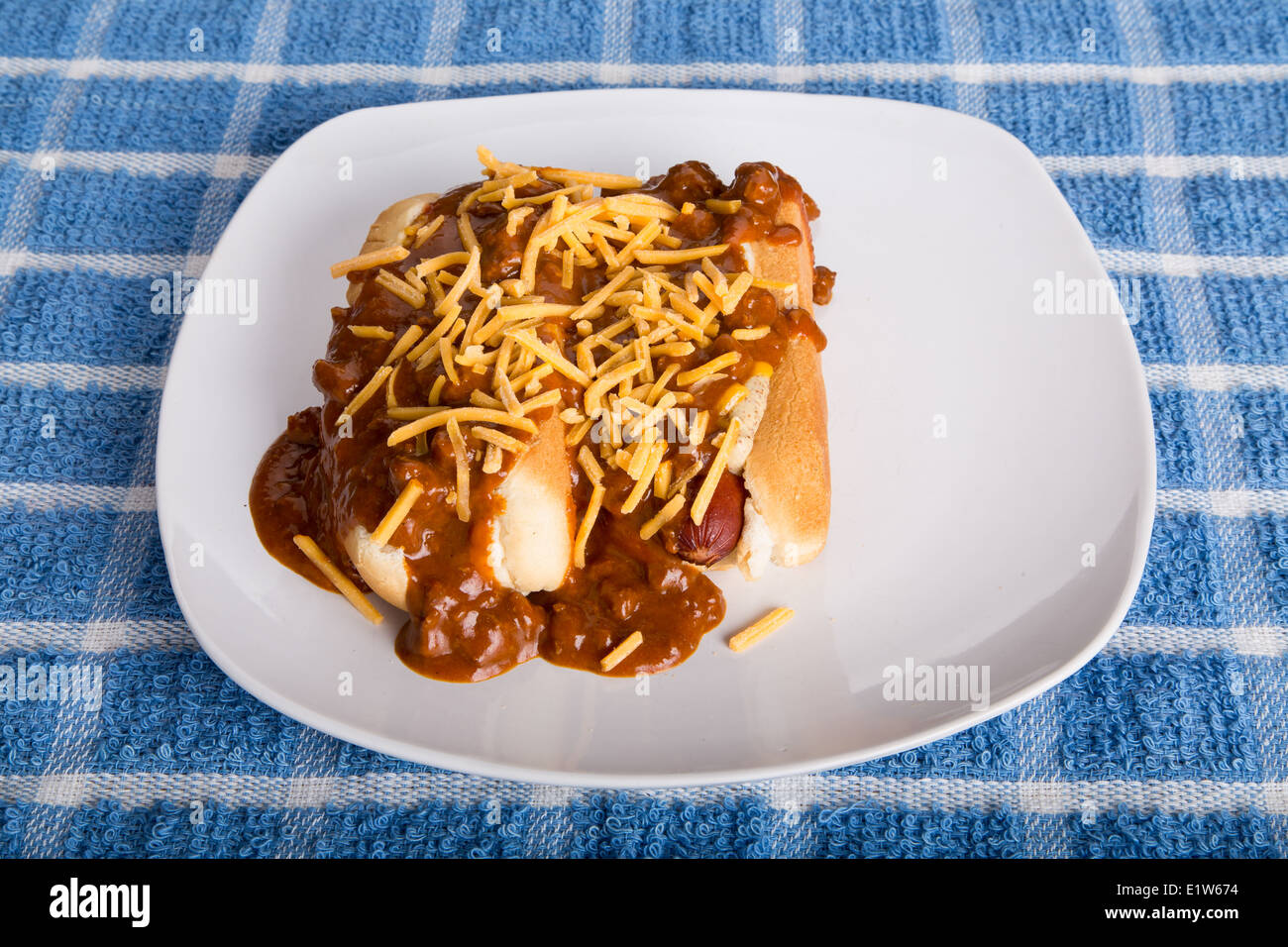 Two hot dogs on a white plate smothered in beef chili and shredded cheddar Cheese Stock Photo