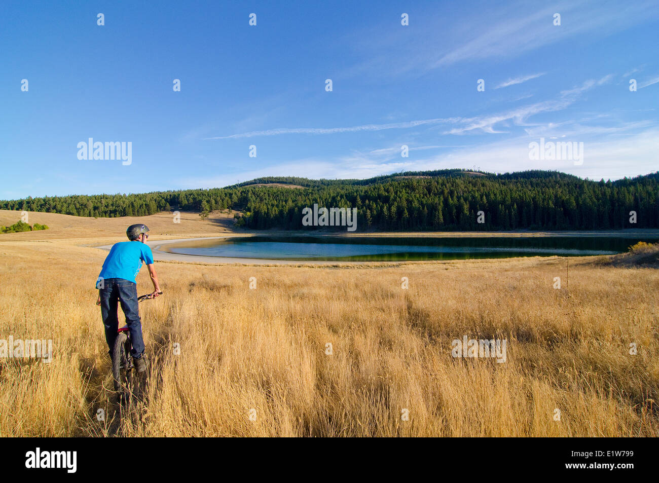 Young mountain biker rides towards unknown lake near Merritt in the Nicola Valley region of British Columbia, Canada Stock Photo