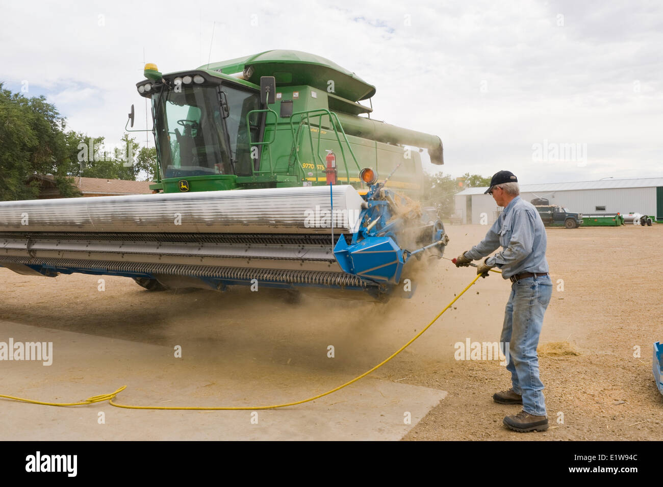 Farmer cleans barley debris from a stripper header on a combine parked in his farmyard, near Ponteix, Saskatchewan, Canada Stock Photo