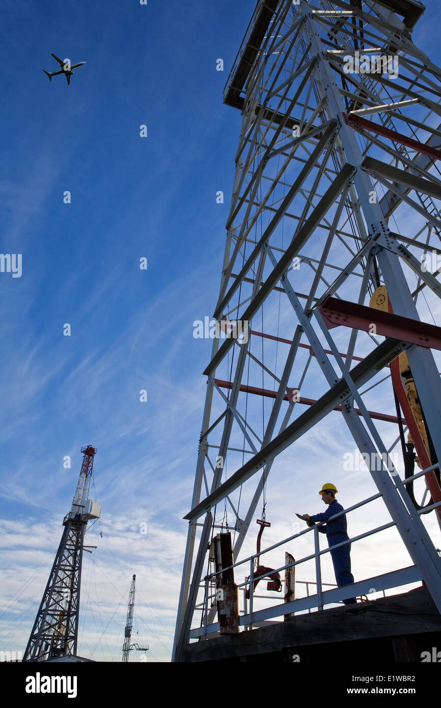 Oil drilling rig worker with airplane flying overhead, Alberta, Canada Stock Photo