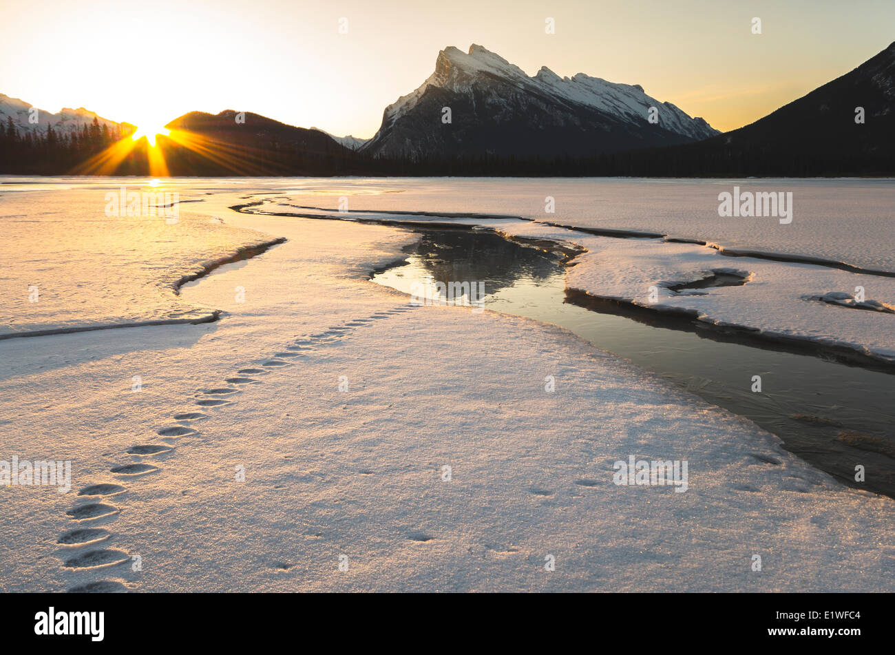 Sun rising beside Mount Rundle reflecting on ice on snow covered Vermilion Lakes in winter in Banff National Park Alberta Stock Photo