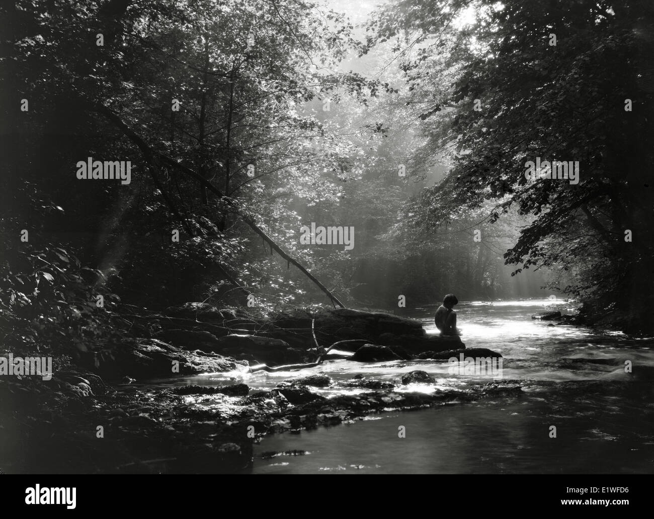 Boy sitting on a rock by a river Stock Photo - Alamy