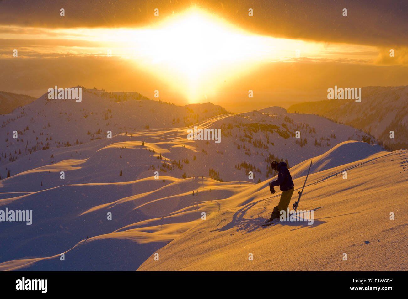 A male skier prepares for a descent at sunrise from a ridgetop of Sol Mountain Monashee Mountains, British Columbia Stock Photo