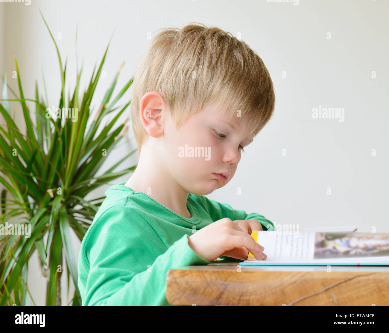 a little boy reading a book at a table Stock Photo
