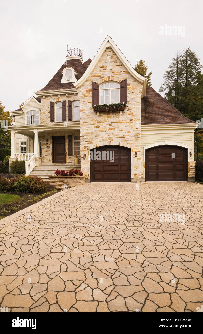 Luxurious brown beige stone cottage style residential home with two car garage paving stone driveway in autumn Quebec Canada. Stock Photo