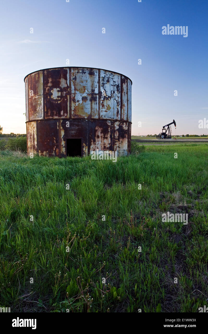 Abandoned oil storage container with working pumpjack in background, Alberta, Canada. Stock Photo