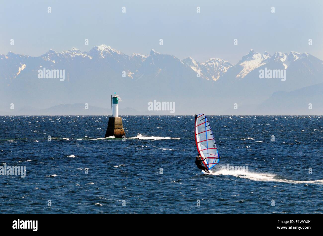 A windsurfer heads towards a marine marker in the Strait of Georgia near Pipers Lagoon in Nanaimo, BC.  The coastal mountains on Stock Photo