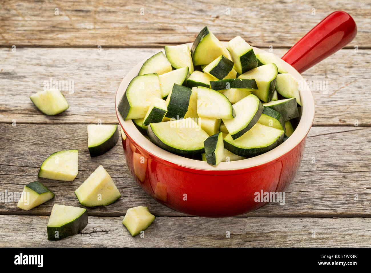 diced and sliced zucchini in red stoneware pot against rustic wooden table Stock Photo