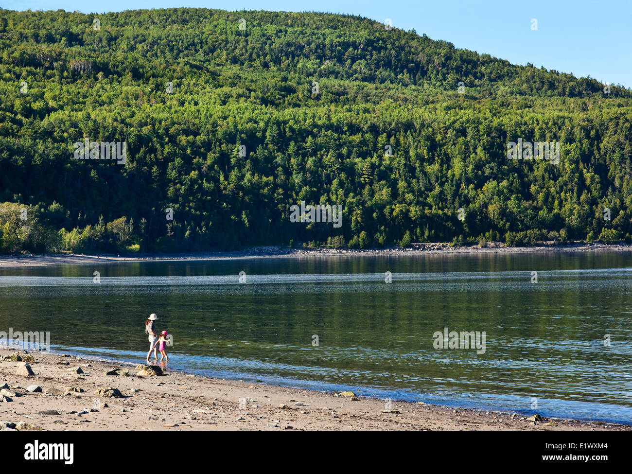 Mother and daughter slowly advancing into the cold water of the St. Lawrence River at a secluded beach in Cap-aux-Oies, Charlevo Stock Photo