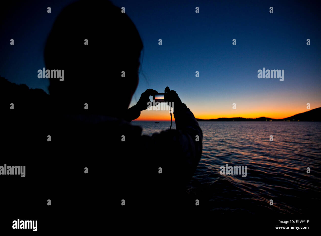 A young woman captures a sunset on her point and shoot in Kalymnos, Greece Stock Photo