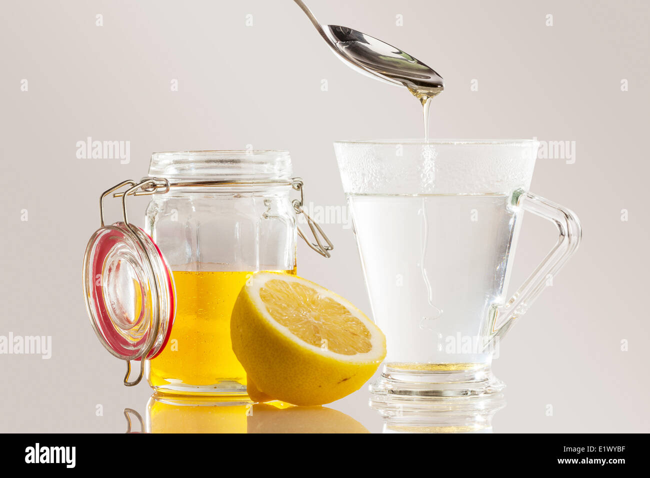 Honey and lemon being mixed into a glass mug of hot water making a soothing drink for a sore throat Stock Photo