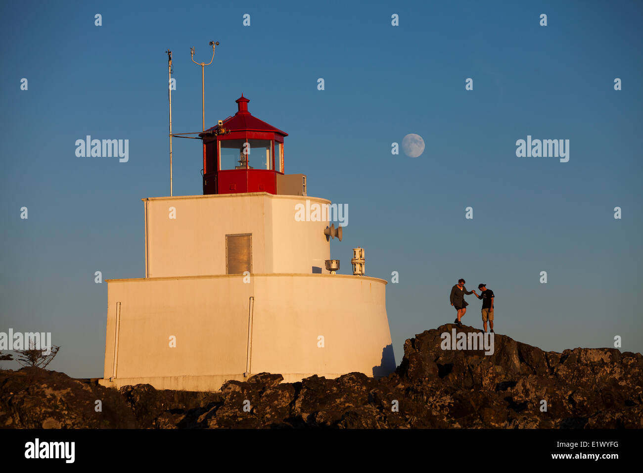 A couple negotiates the rocky headland surrounding the Amphrite Lighthouse in Ucluelet. The Wild Pacific Trail Ucluelet Stock Photo