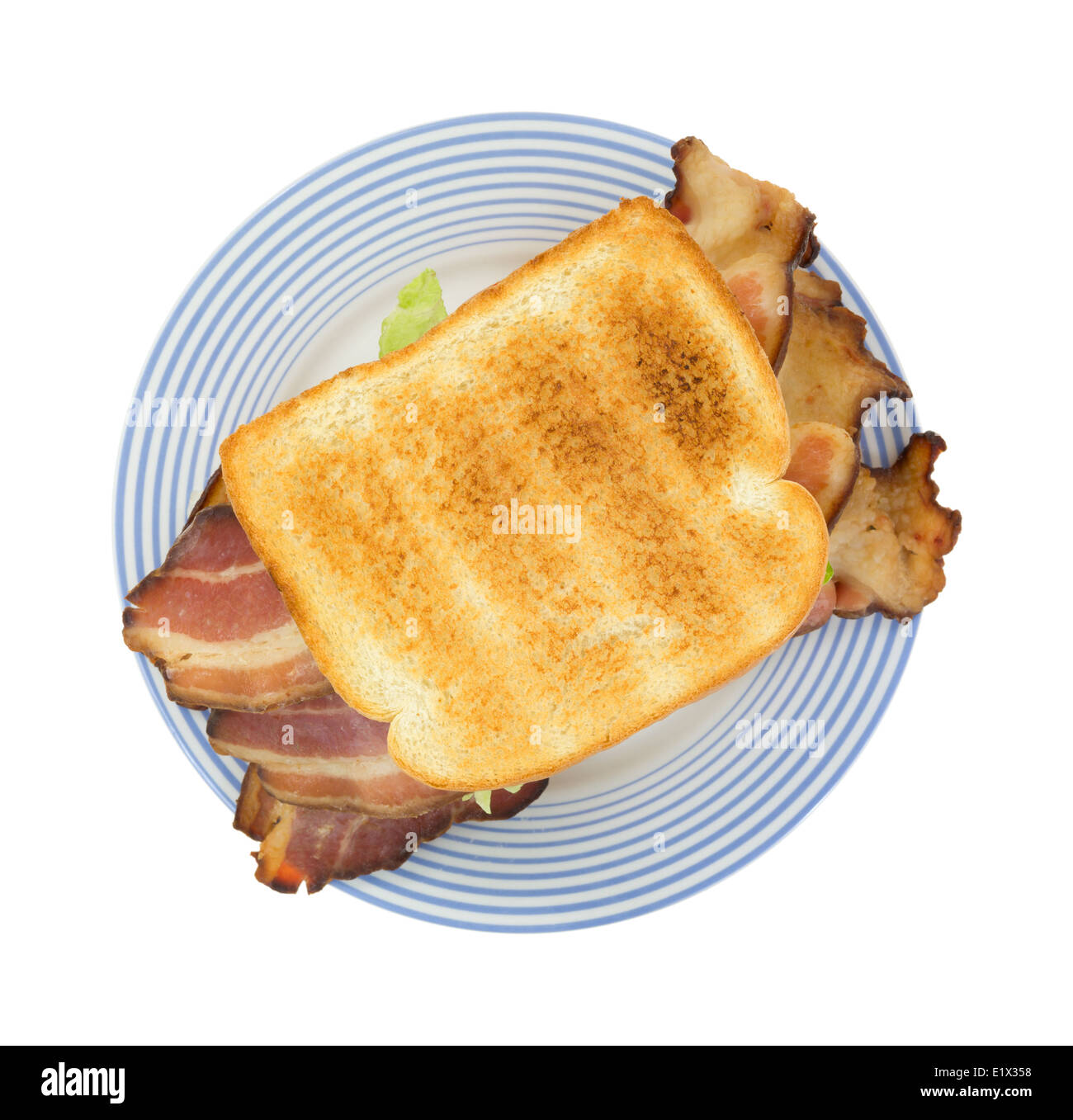 Top view of a large bacon sandwich with lettuce on an old blue striped plate. Stock Photo