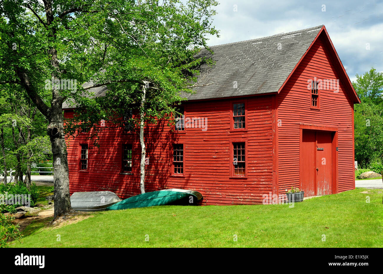Two wooden rowboats lie next to a bright red barn in the historic mill town of Harrisville, New Hampshire Stock Photo