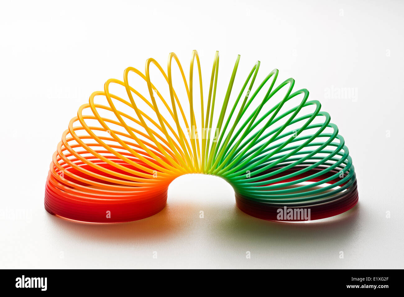 Rainbow colored slinky toy made of a plastic wire spiral coil which enables flexibility and mobility Stock Photo