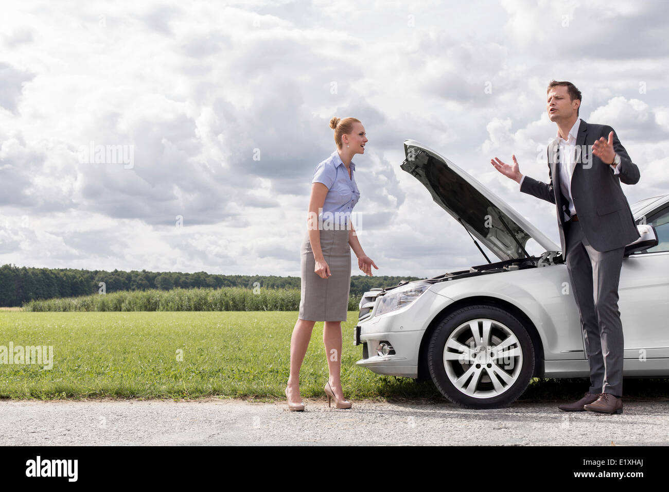 Full length of business couple having argument by broken car at countryside Stock Photo