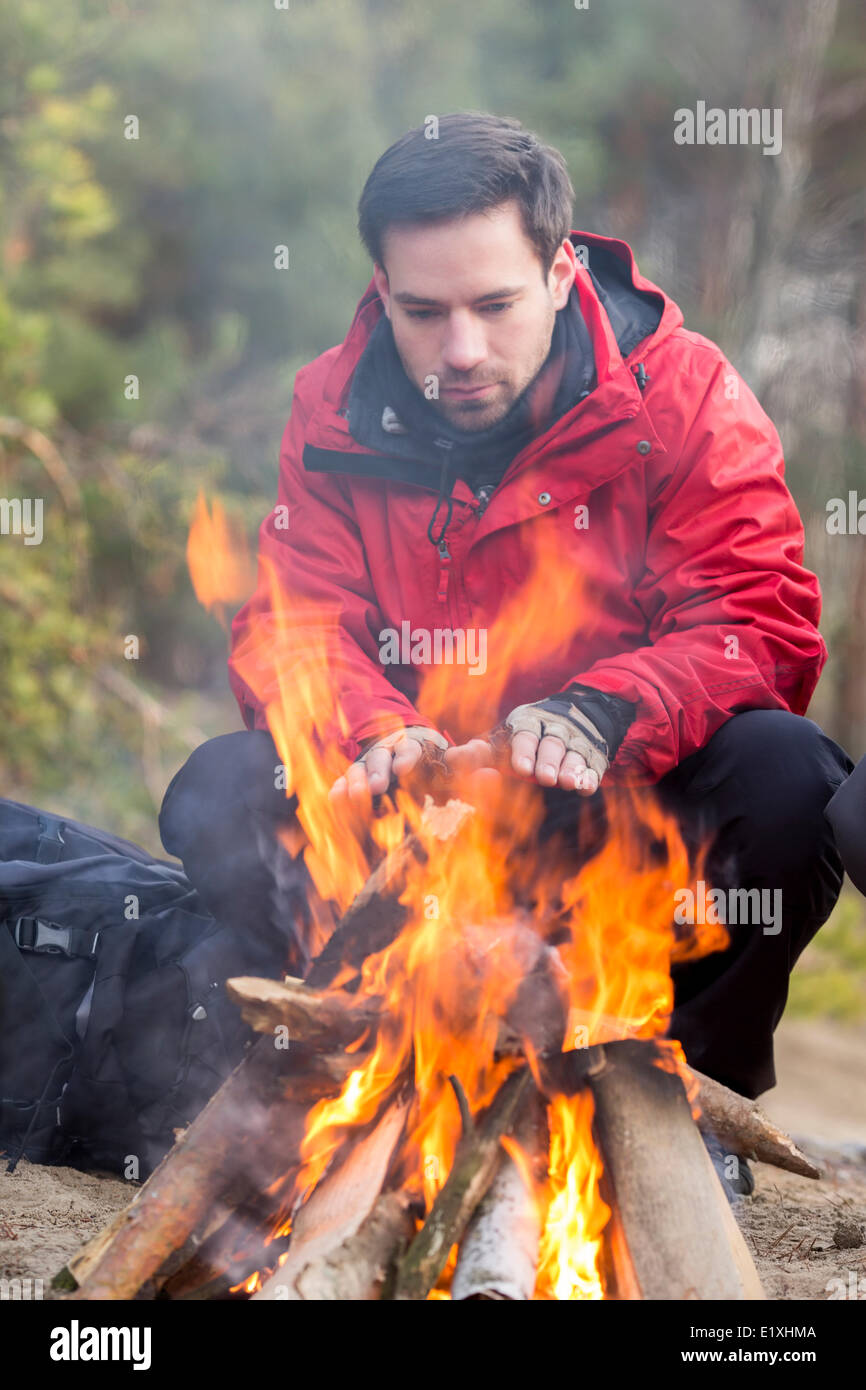 Male hiker warming his hands at campfire in forest Stock Photo