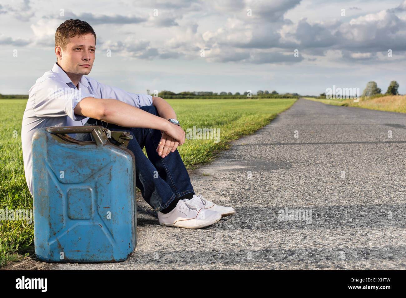 Full length of young man with empty gas can sitting by road Stock Photo