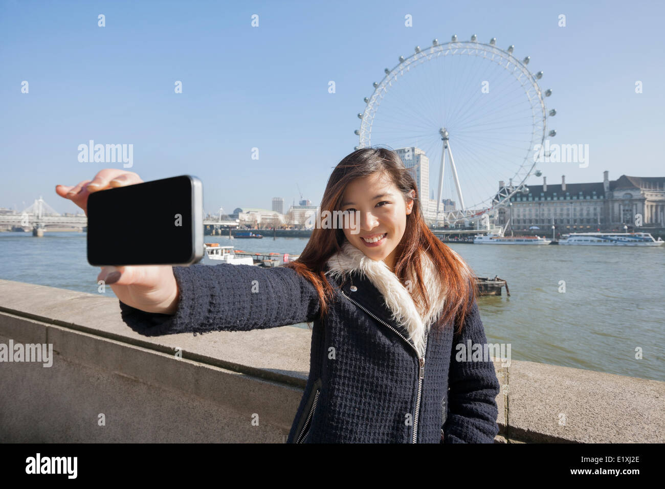 Portrait woman taking self portrait through cell phone against London Eye at London, England, UK Stock Photo