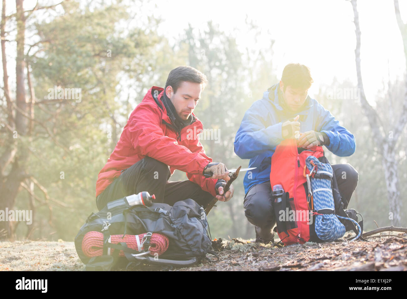 Male backpacker with friend whittling wood in forest Stock Photo