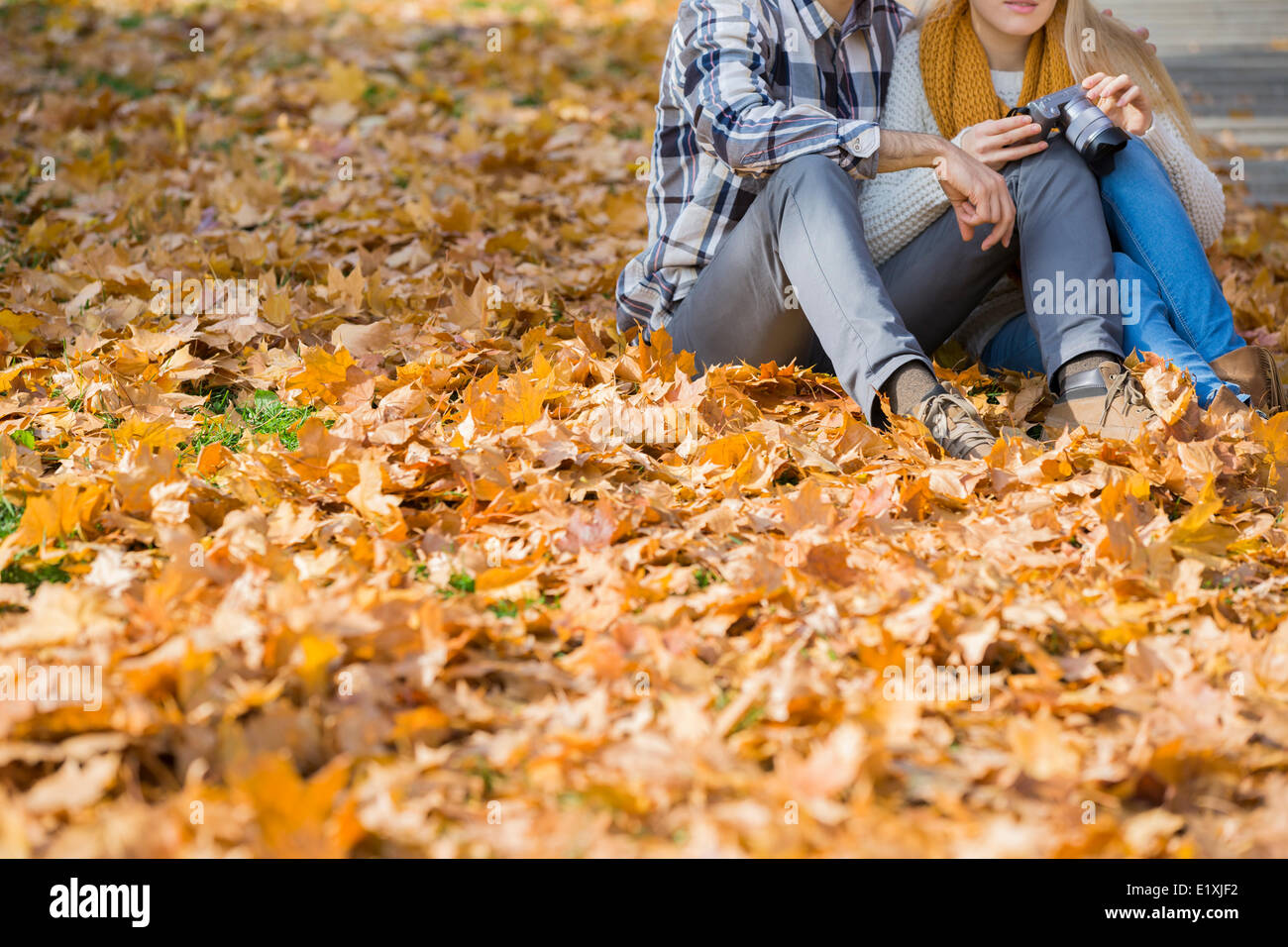 Low section of couple with camera sitting on autumn leaves in park Stock Photo