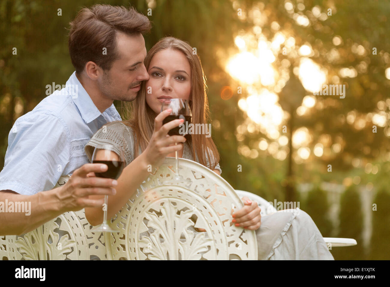 Romantic young couple having red wine on chairs in park Stock Photo - Alamy