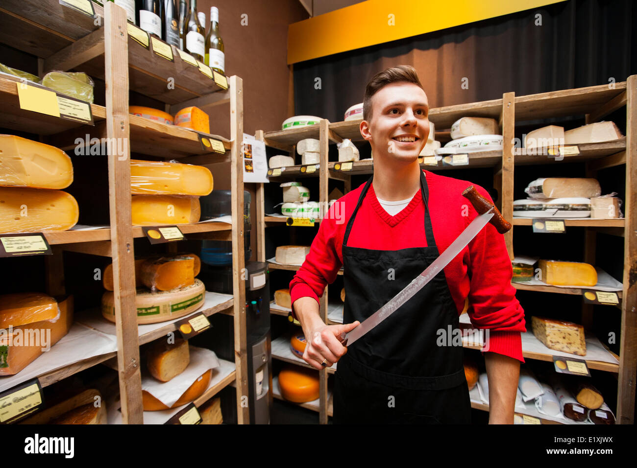 Smiling male salesperson holding knife in cheese store Stock Photo