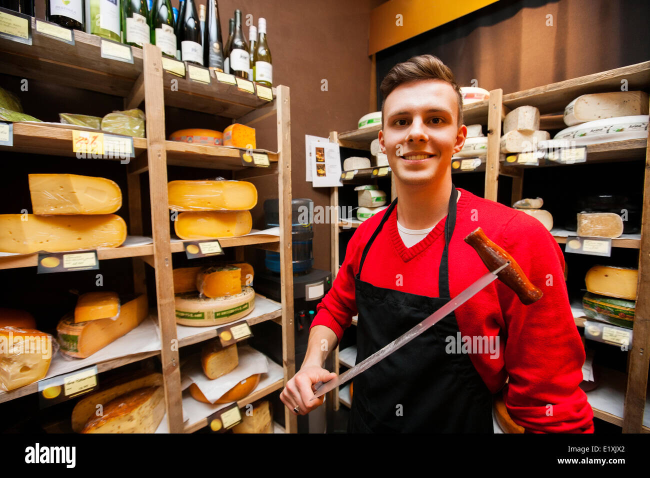 Portrait of confident male salesperson holding knife in cheese store Stock Photo