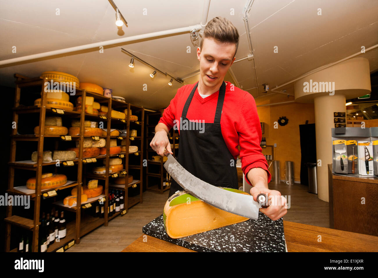 Young store clerk cutting cheese at counter Stock Photo