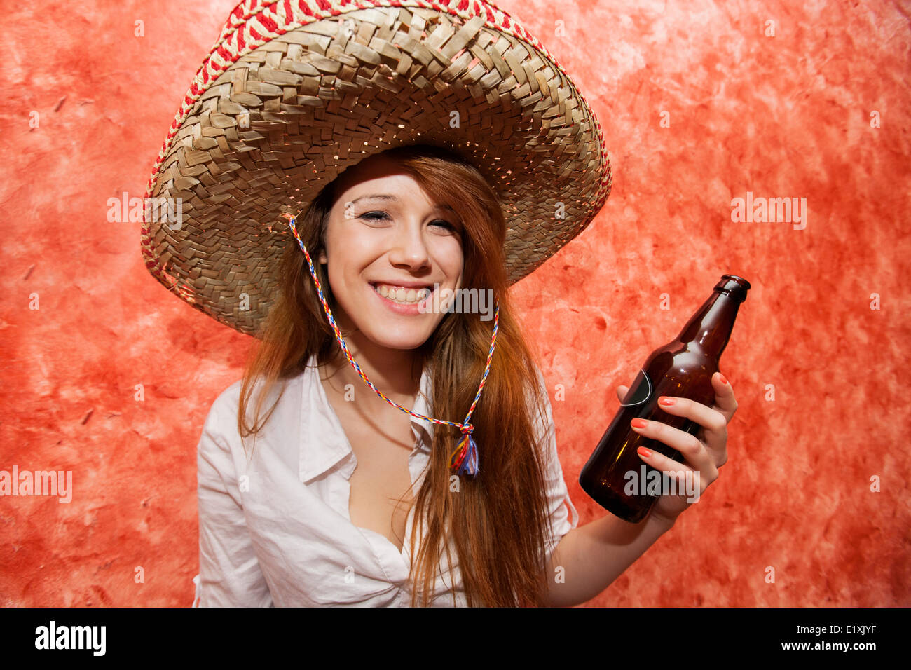 Happy woman in Mexican hat holding beer bottle in restaurant Stock Photo