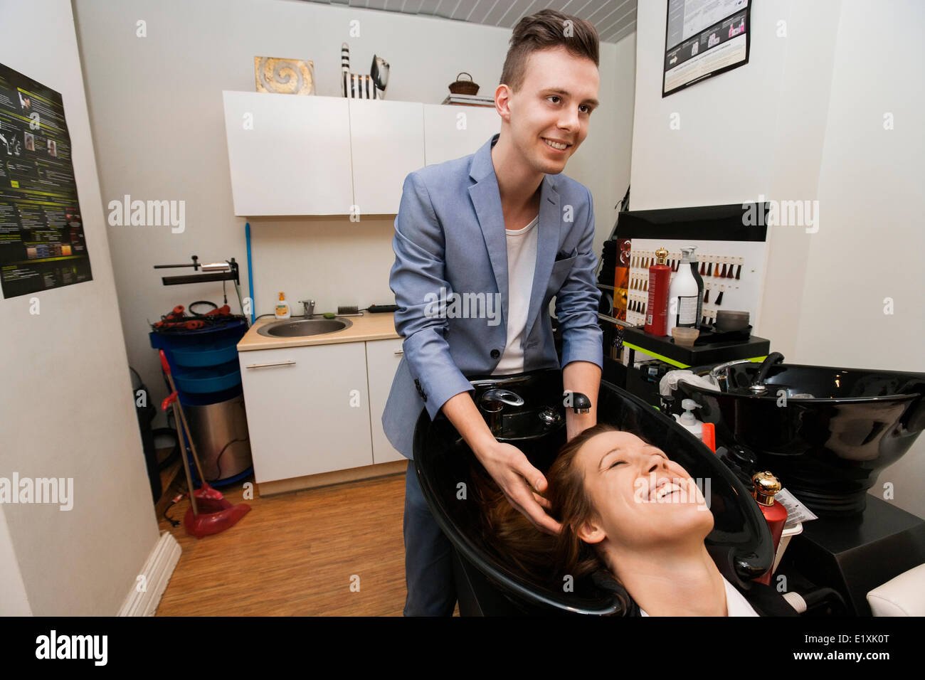 Smiling male hairstylist washing female customer's hair in salon Stock Photo