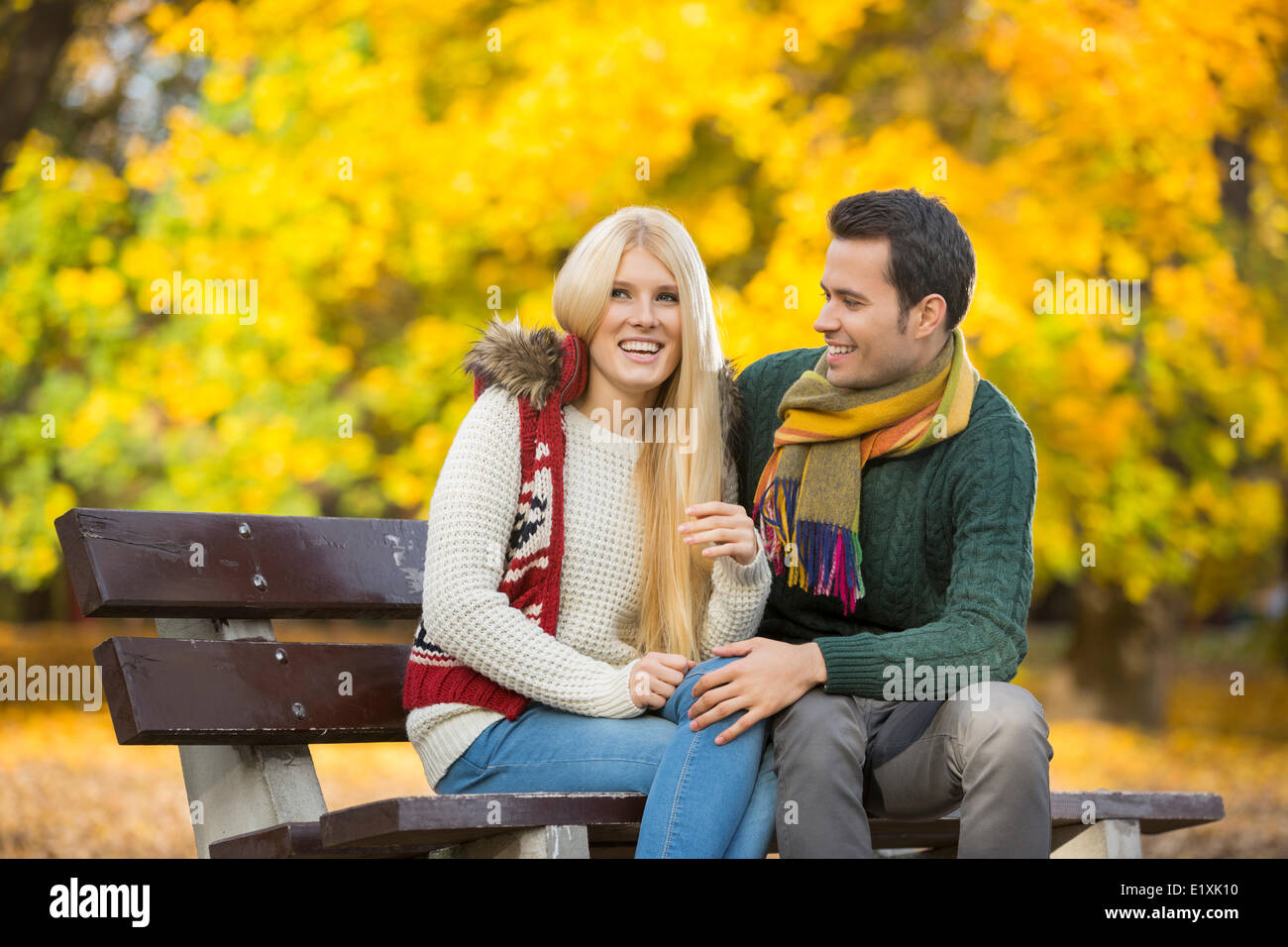 Happy young couple sitting on park bench during autumn Stock Photo - Alamy