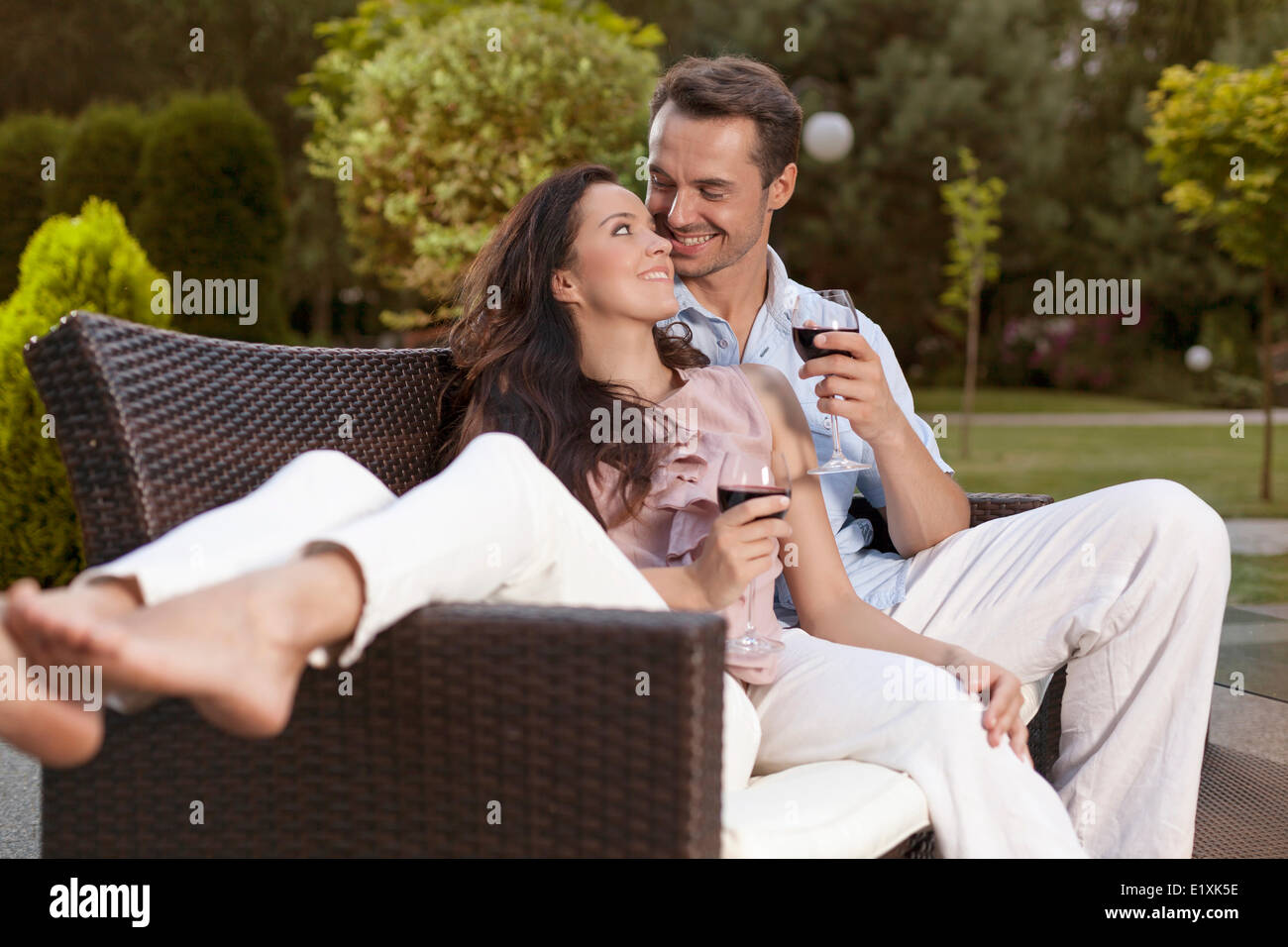 Romantic young holding wine glasses on easy chair in park Stock Photo