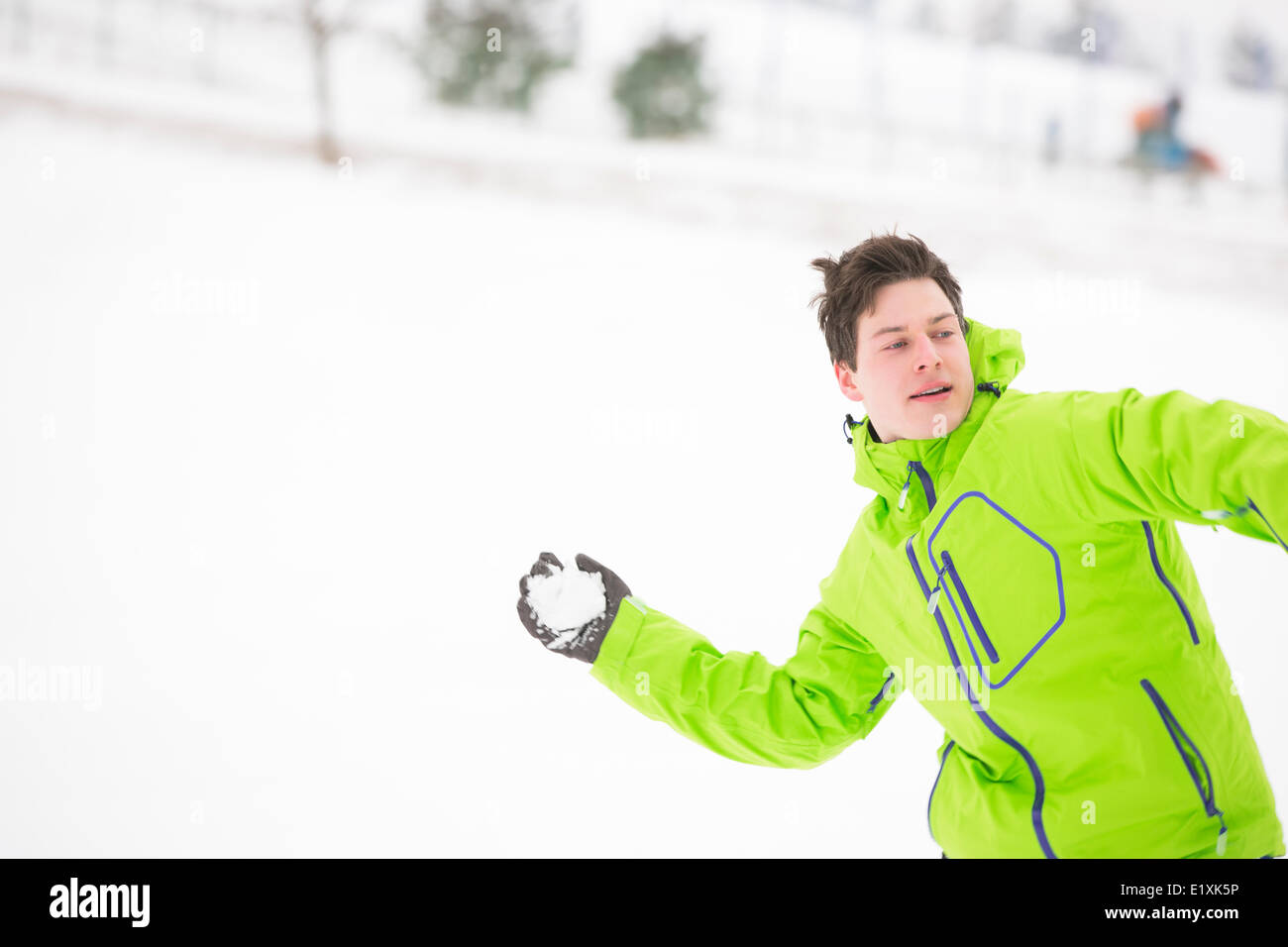 Young man in hooded jacket throwing snowball Stock Photo
