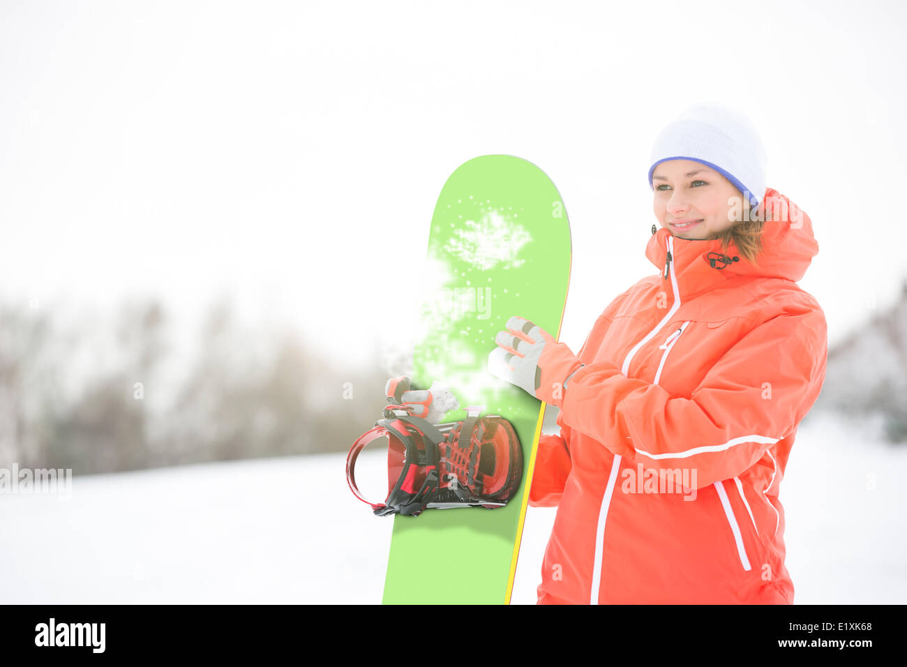 Happy young woman looking away while holding snowboard in snow Stock Photo