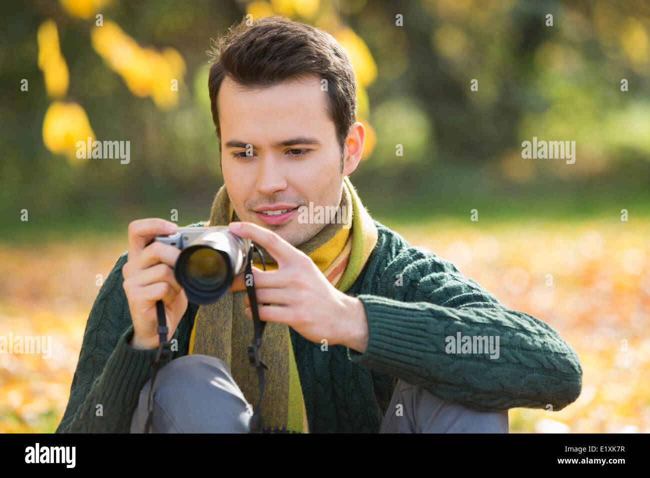 Young man watching photographs on digital camera in park during autumn Stock Photo