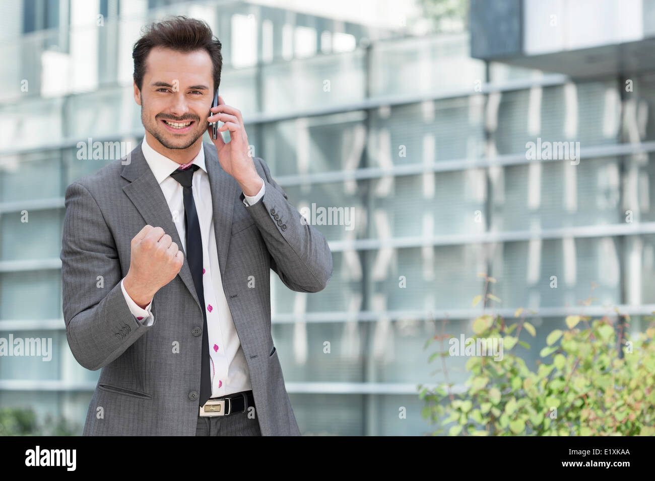 Portrait of successful young businessman using cell phone against office building Stock Photo