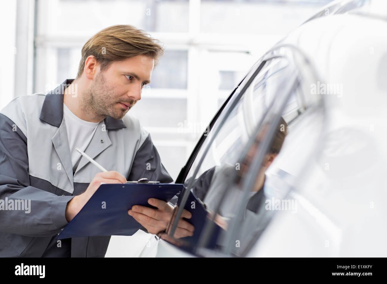 Mid adult repair worker writing on clipboard while examining car in workshop Stock Photo