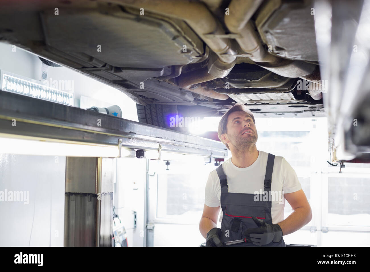 Mid adult male automobile mechanic worker examining car in workshop Stock Photo