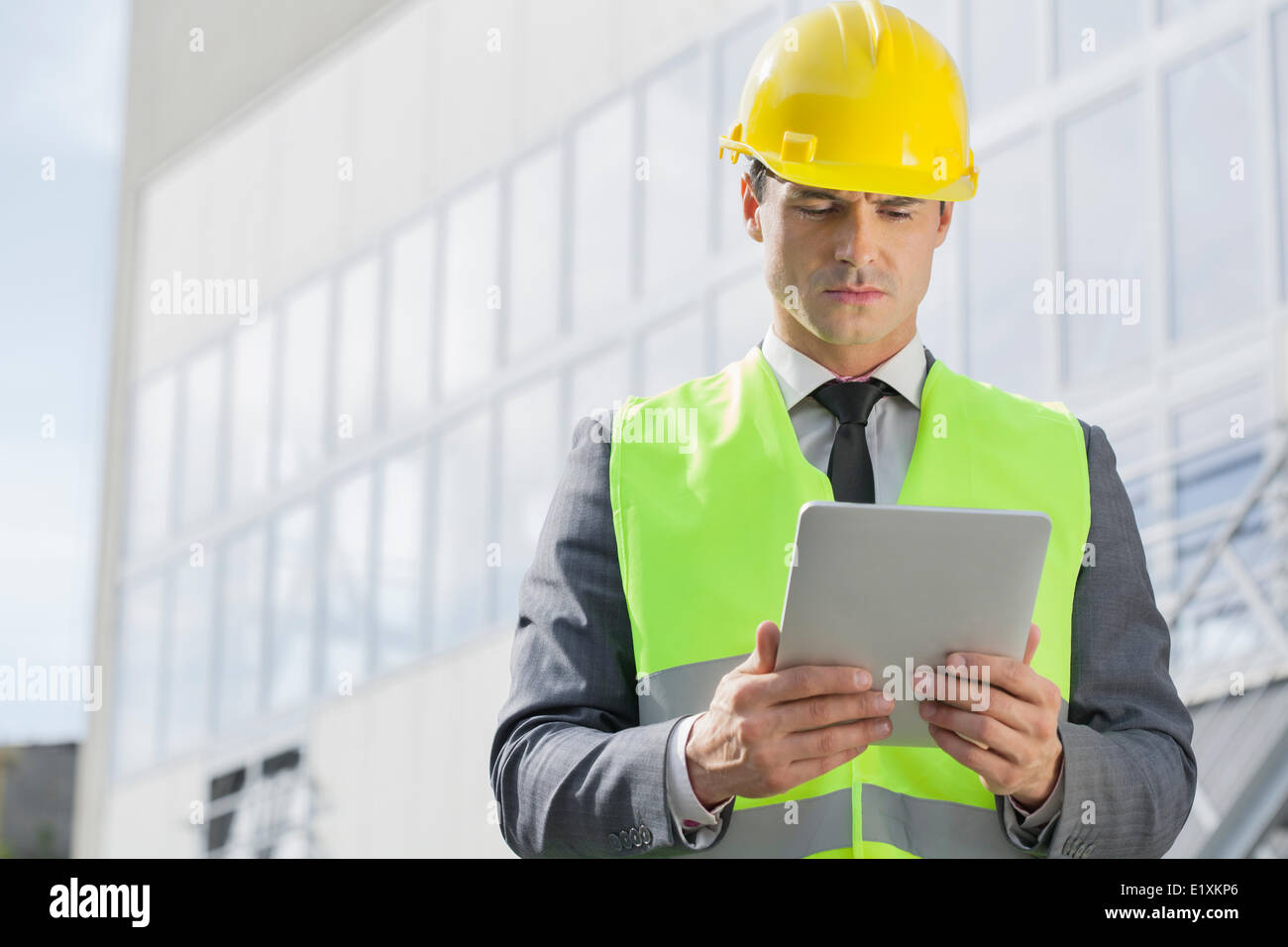 Young male engineer in reflector-vest and hardhat using digital tablet outside industry Stock Photo