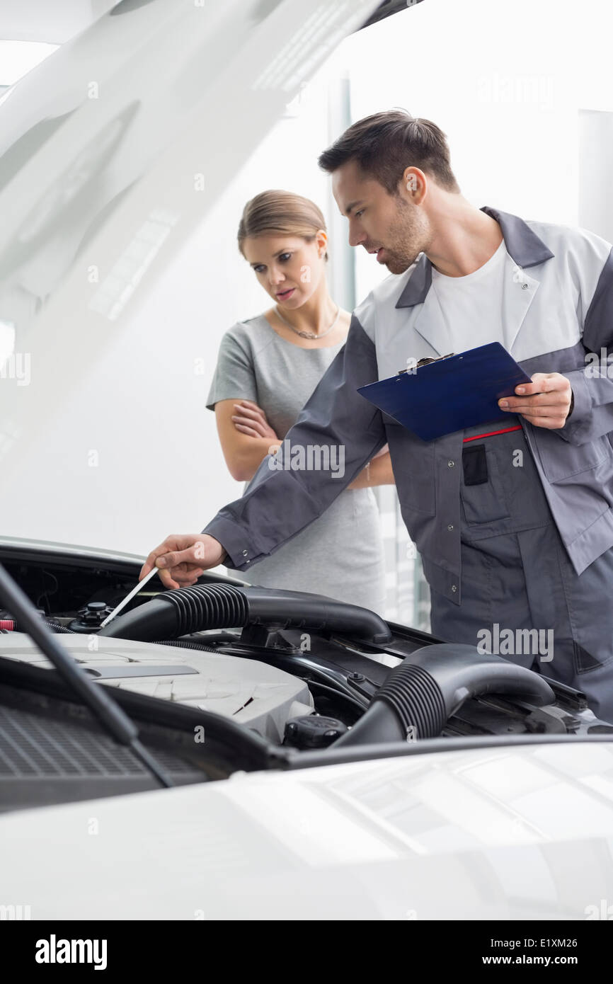 Male maintenance engineer explaining car engine to female customer in