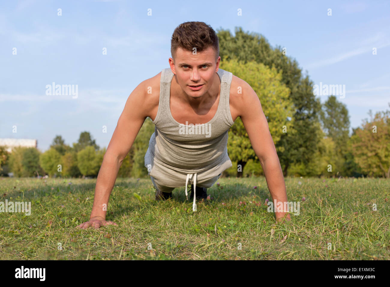Portrait of young man doing pushups in park Stock Photo - Alamy