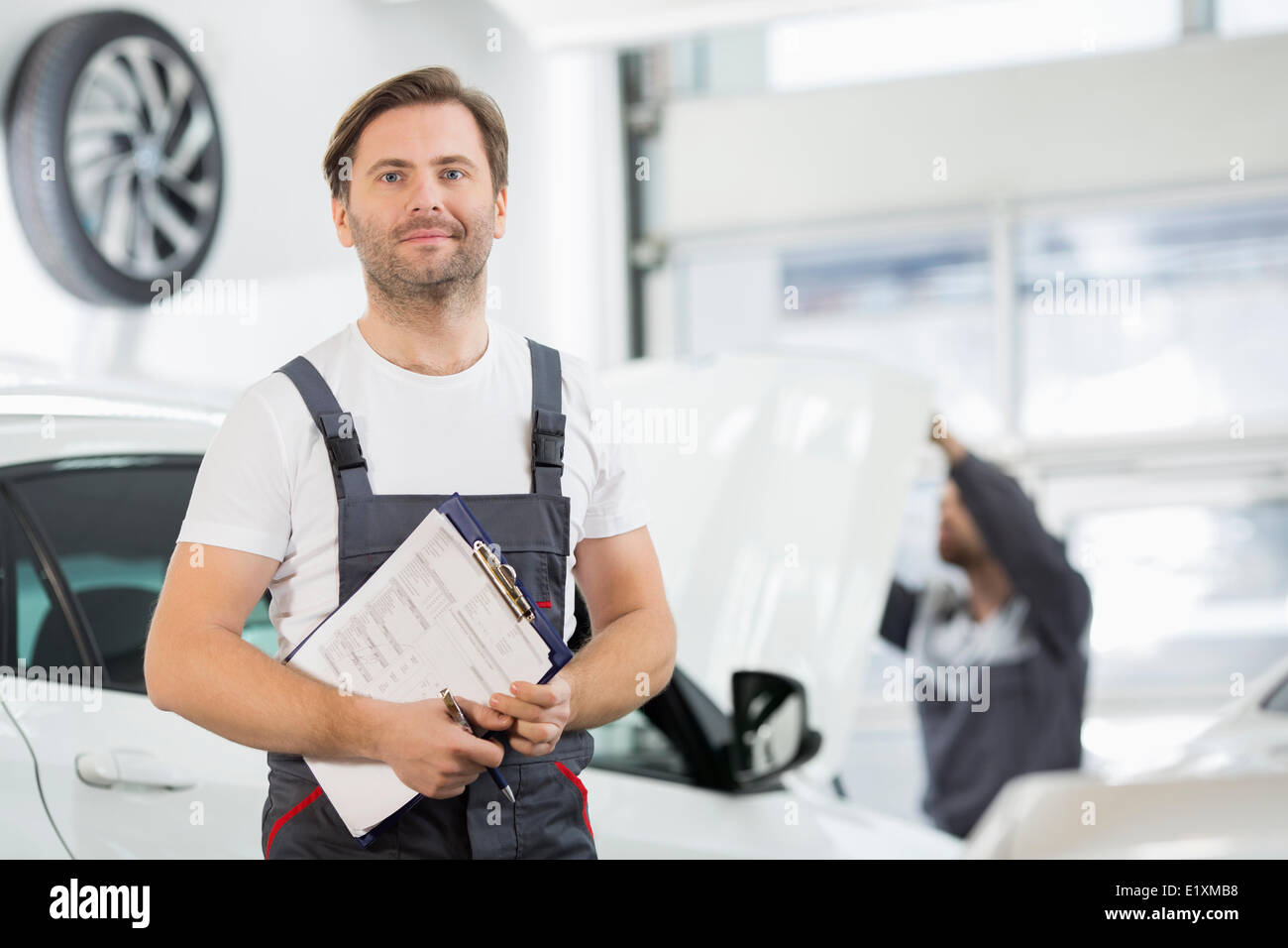 Portrait of confident male maintenance engineer with clipboard in car repair shop Stock Photo
