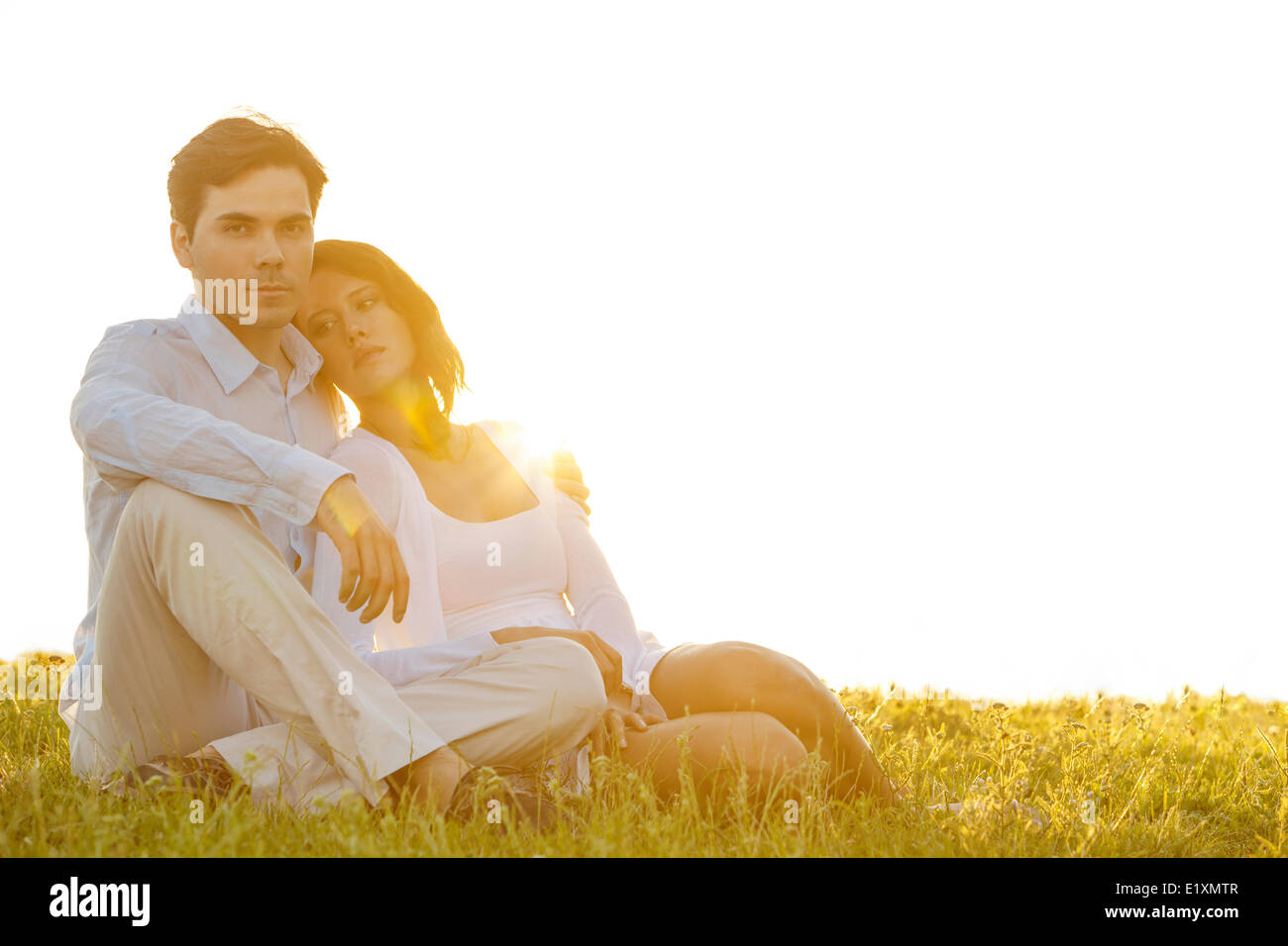 Portrait of confident young man sitting with girlfriend on grass against clear sky Stock Photo